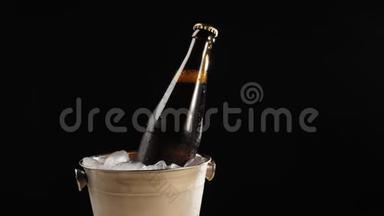 新鲜啤酒。 手拿一个棕色的瓶子和美味的工艺啤酒，从一个桶里拿出来，在黑色的背景下放着冰冷的真正的冰。
